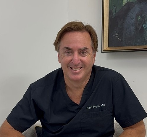 Smiling doctor in scrubs seated in office.