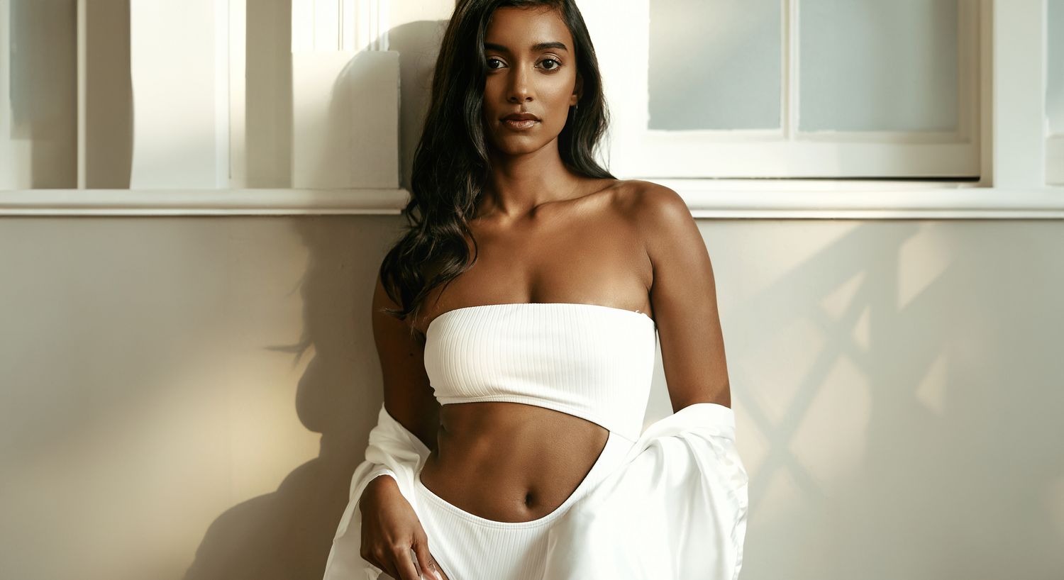 Model in white outfit posing by window.