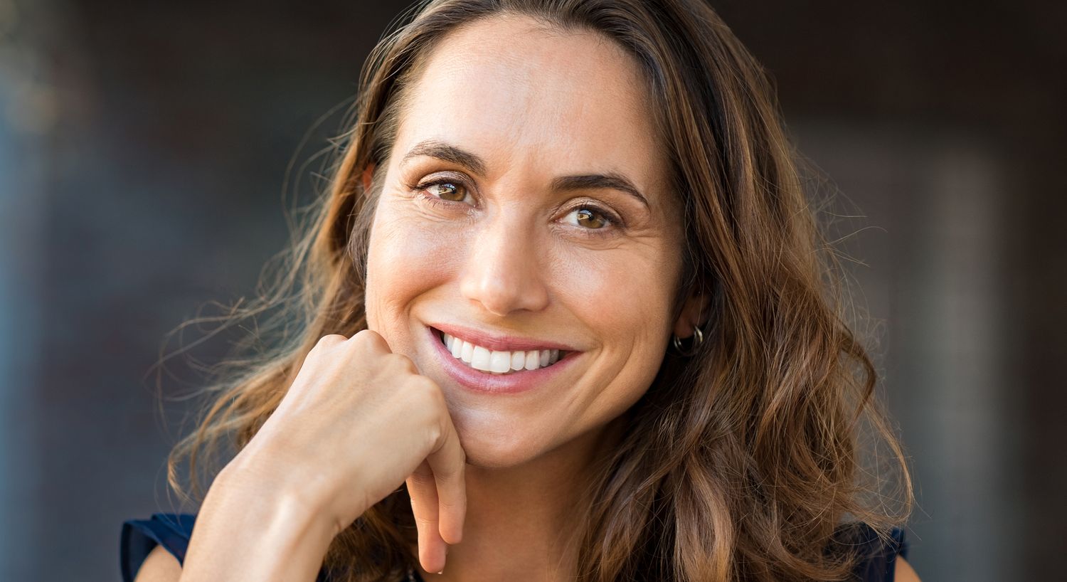 Smiling woman with long hair resting chin.