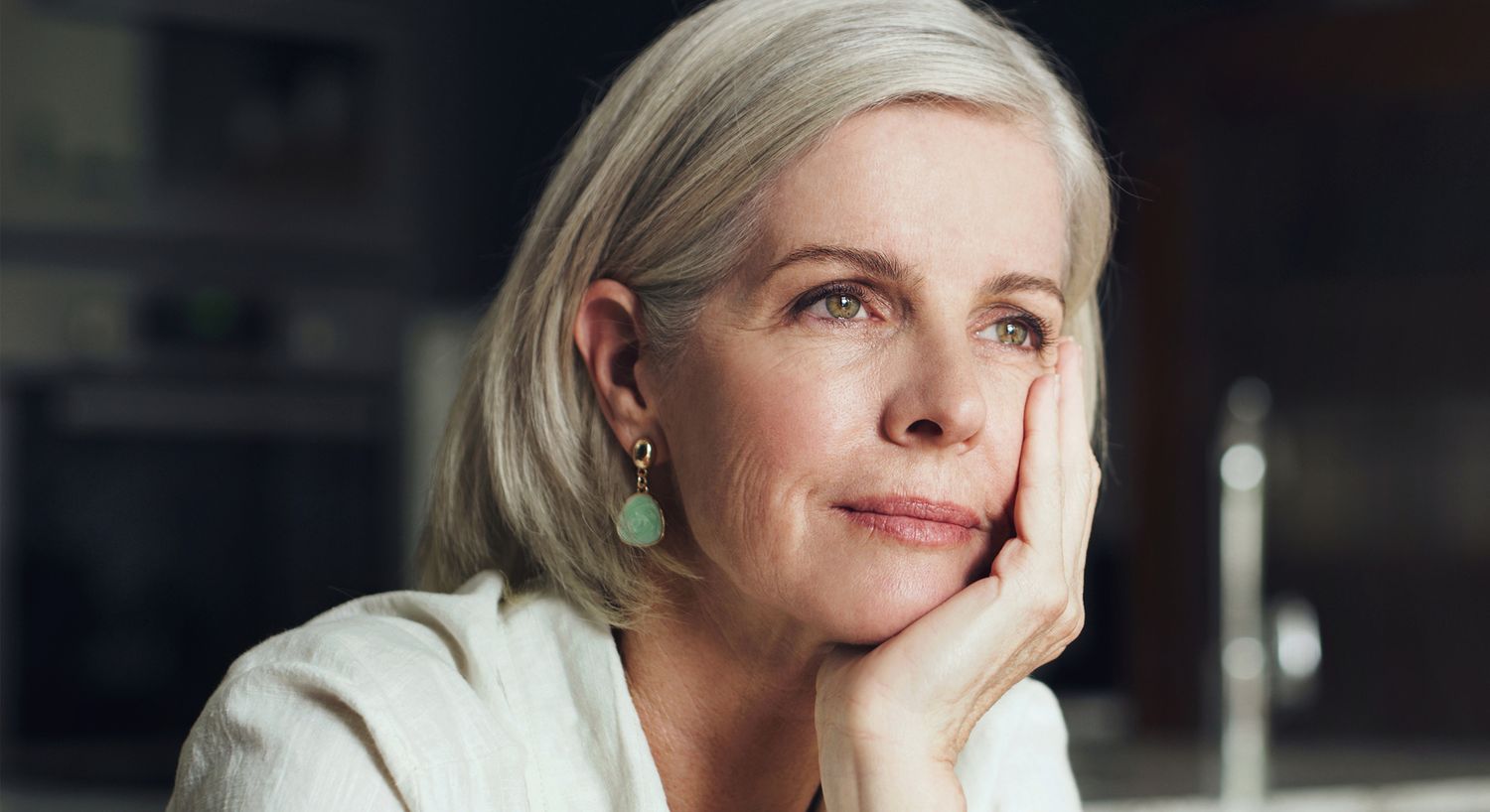 Thoughtful woman with gray hair and green earrings.