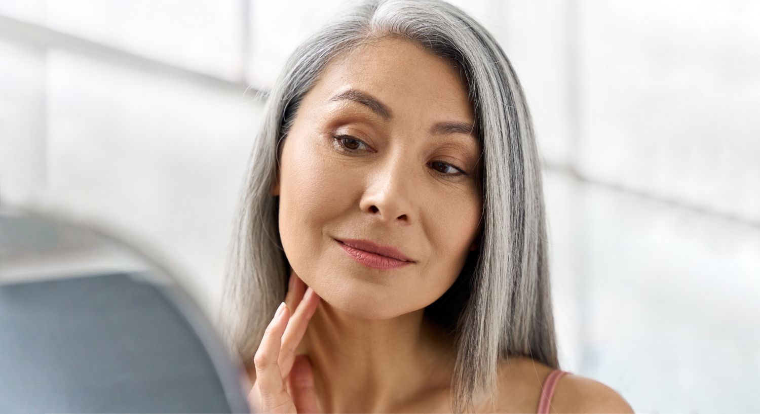 Woman with gray hair looking in mirror.